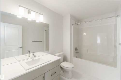 Contemporary bathroom featuring a light gray vanity with a single basin sink and chrome faucet, a large wall-mounted mirror, and a white bathtub with a shower kit - 19360 29 Avenue, Edmonton, AB 