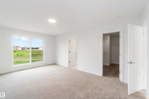 Bright interior room featuring a large window, light-colored carpeting, a circular ceiling light fixture, a closet with wire shelving, and white paneled doors - 19360 29 Avenue, Edmonton, AB 