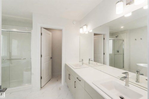 Spacious bathroom featuring a double vanity with integrated sinks, a large wall-mounted mirror, and a glass-enclosed shower - 19360 29 Avenue, Edmonton, AB 
