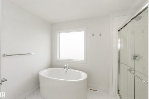 Freestanding oval soaking tub with deck-mounted chrome fixtures, accompanied by a glass-enclosed shower with subway tile surround and chrome hardware - 19360 29 Avenue, Edmonton, AB 