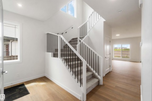 Inviting foyer featuring wood-finish flooring, a contemporary staircase with black spindles and white railings, and a prominent skylight - 19360 29 Avenue, Edmonton, AB 