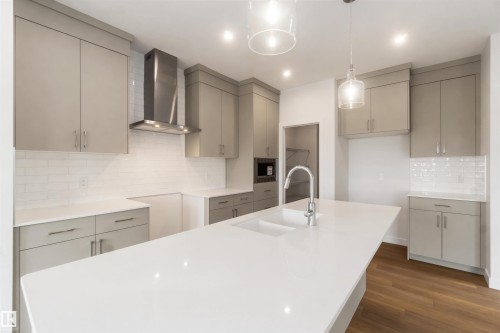 Spacious kitchen featuring an expansive island with an integrated sink, light gray cabinetry, white countertops, and a white subway tile backsplash - 19360 29 Avenue, Edmonton, AB 