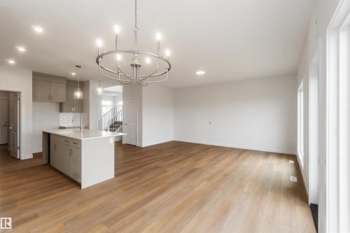 Open-concept main level featuring wood-finish flooring, a contemporary kitchen island with a white countertop and undermount sink, pendant lighting, and a modern chandelier - 19360 29 Avenue, Edmonton, AB 