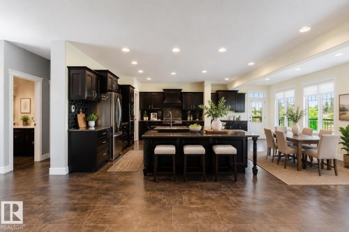 Open-concept kitchen and dining area featuring dark wood cabinetry, stainless steel appliances, a large central island with seating, and ceramic tile flooring - 3438 West Landing Landing, Edmonton, AB 