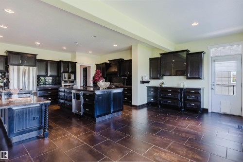 Spacious kitchen featuring dark wood cabinetry, a large center island with built-in appliances, a second island with an integrated sink, stainless steel appliances, and tile flooring - 3438 West Landing Landing, Edmonton, AB 