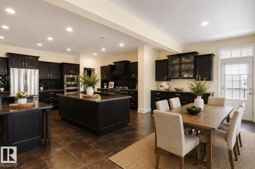 Open-concept kitchen and dining area featuring dark cabinetry, stainless steel appliances, two kitchen islands with solid surface countertops, recessed lighting, and a glass-paneled door - 3438 West Landing Landing, Edmonton, AB 