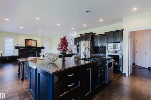 Kitchen featuring dark cabinetry, stainless steel appliances, granite countertops, and a large central island with an integrated sink - 3438 West Landing Landing, Edmonton, AB 