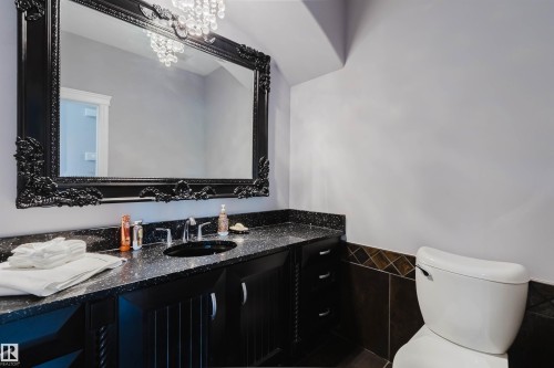 Bathroom featuring a large ornate black framed mirror, a black countertop with integrated sink, black cabinetry, a crystal chandelier, and wall tiling - 3438 West Landing Landing, Edmonton, AB 