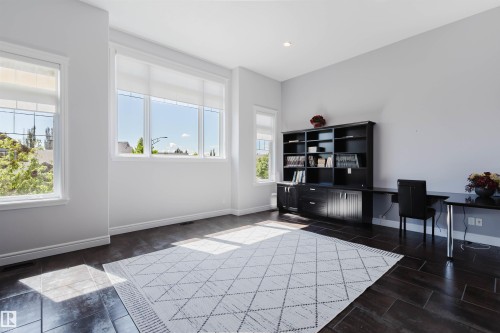 Spacious room featuring dark wood-finish flooring, a built-in dark wood bookcase with integrated desk, multiple large windows, recessed lighting, and crisp white baseboards - 3438 West Landing Landing, Edmonton, AB 