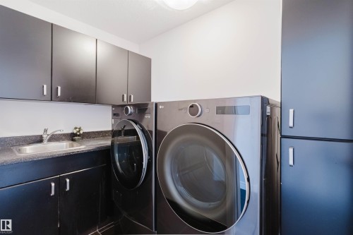 Laundry area featuring dark cabinetry, a countertop with an integrated sink, and modern appliances - 3438 West Landing Landing, Edmonton, AB 