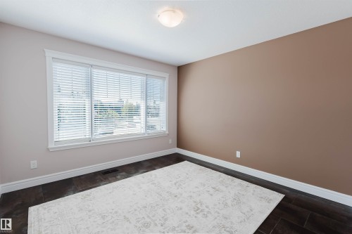 Spacious room featuring dark wood-look flooring, a large window with white blinds, and a neutral color palette - 3438 West Landing Landing, Edmonton, AB 