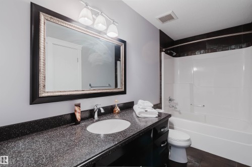 Bathroom featuring a spacious vanity with a dark speckled countertop, an undermount sink, and a framed mirror with overhead lighting - 3438 West Landing Landing, Edmonton, AB 