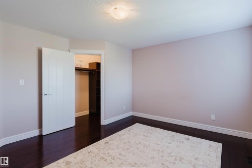 Spacious room featuring dark wood-finish flooring, light-colored walls, and a built-in closet with shelving and hanging rods - 3438 West Landing Landing, Edmonton, AB 