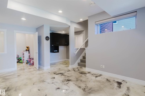 Spacious room featuring modern epoxy flooring, recessed lighting, a built-in dark wood-finish cabinet system, and a carpeted staircase with a white handrail - 3438 West Landing Landing, Edmonton, AB 