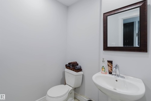 Bathroom featuring a pedestal sink, chrome faucet, wall-mounted mirror with a dark wood frame, and a white toilet - 3438 West Landing Landing, Edmonton, AB 