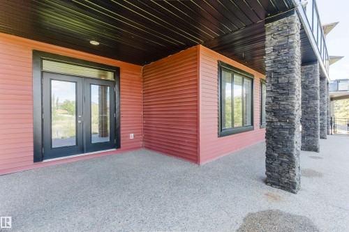 Lower-level patio featuring exposed aggregate concrete flooring and a red horizontal siding exterior - 3438 West Landing Landing, Edmonton, AB 