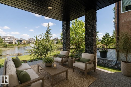 Covered patio featuring stacked stone pillars, recessed lighting, and a durable aggregate surface overlooking a serene pond with a water feature and surrounding residences - 3438 West Landing Landing, Edmonton, AB 