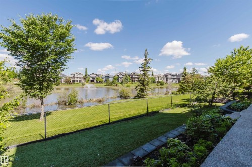 Landscaped backyard featuring a manicured lawn, established trees, and a chain-link fence bordering a pond with a fountain - 3438 West Landing Landing, Edmonton, AB 