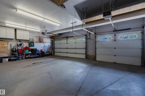 Attached two-car garage featuring segmented overhead doors with integrated windows, concrete flooring, and overhead fluorescent lighting - 3438 West Landing Landing, Edmonton, AB 