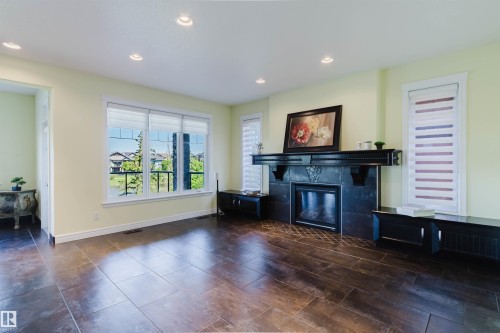 Spacious room featuring large format tile flooring, a prominent fireplace with a dark stone surround and mantel, and multiple windows with white trim - 3438 West Landing Landing, Edmonton, AB 