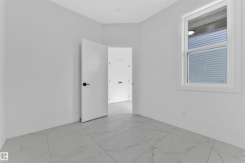 Bright room featuring white walls, large white-framed window, modern white door with matte black hardware, and large format porcelain tile flooring - 4409 35 Street, Beaumont, AB - Indoor Photo Showing Other Room