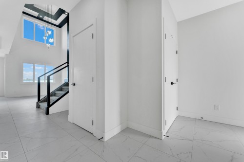Two-story entry foyer featuring a modern staircase with glass railing, large format tile flooring, and a contemporary chandelier - 4409 35 Street, Beaumont, AB - Indoor Photo Showing Other Room