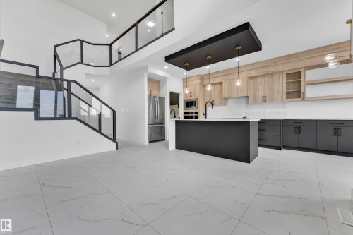 Spacious open-concept interior featuring light-toned tile flooring, a modern kitchen with a dark-toned island, light wood-finish cabinetry, and built-in stainless steel appliances - 4409 35 Street, Beaumont, AB - Indoor Photo Showing Kitchen