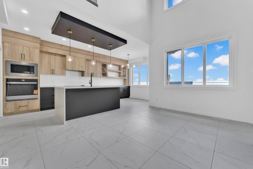 Modern kitchen featuring light wood-finish cabinetry and a dark island with a waterfall countertop - 4409 35 Street, Beaumont, AB - Indoor Photo Showing Kitchen