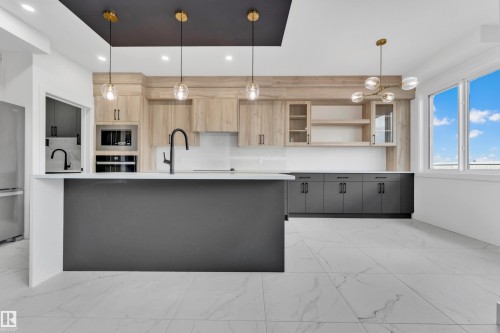 Modern kitchen featuring a large central island, light wood-finish cabinetry, dark base cabinetry, and stainless steel appliances - 4409 35 Street, Beaumont, AB - Indoor Photo Showing Kitchen With Upgraded Kitchen