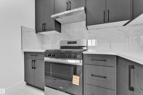 Modern kitchen featuring dark grey cabinetry with matte black hardware, white countertops, and a white marble-look tile backsplash - 4409 35 Street, Beaumont, AB - Indoor Photo Showing Kitchen