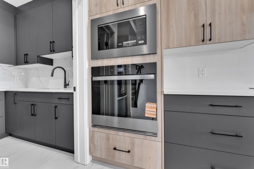 Modern kitchen featuring built-in stainless steel appliances, two-tone cabinetry with matte black hardware, white countertops, and a white tile backsplash - 4409 35 Street, Beaumont, AB - Indoor Photo Showing Kitchen
