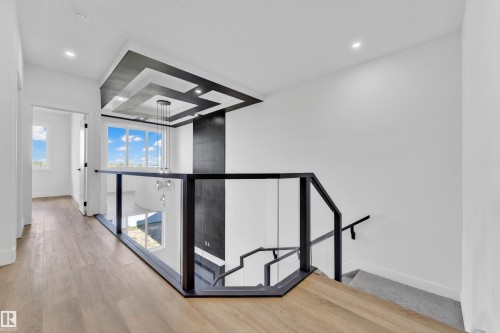 Modern architectural design featuring a multi-level ceiling with recessed lighting, a contemporary chandelier, and a glass-paneled railing - 4409 35 Street, Beaumont, AB - Indoor Photo Showing Other Room