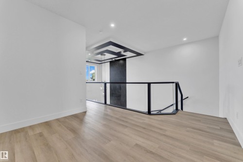 Open landing area featuring wood-finish flooring, recessed lighting, and a modern glass and metal railing system - 4409 35 Street, Beaumont, AB - Indoor Photo Showing Other Room