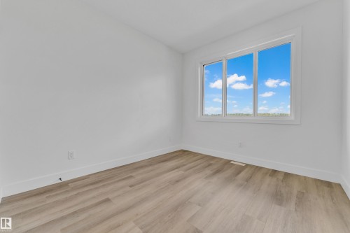 Bright room featuring a large three-panel window, light wood-finish flooring, and crisp white walls - 4409 35 Street, Beaumont, AB - Indoor Photo Showing Other Room