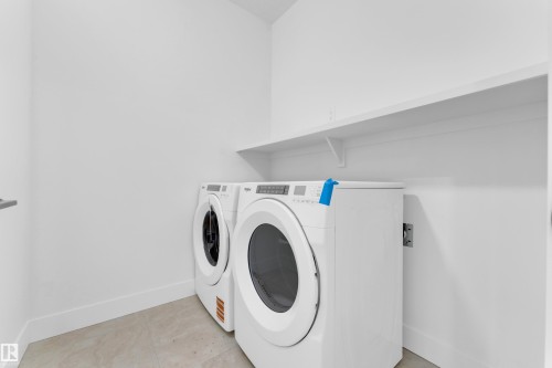 Dedicated laundry area featuring front-loading appliances, a built-in wall shelf, clean white walls, and a light-toned tile floor - 4409 35 Street, Beaumont, AB - Indoor Photo Showing Laundry Room