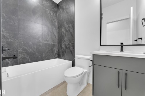 Contemporary bathroom featuring a deep soaking tub with dark marble-look tile surround, a sleek white vanity with a light countertop, a rectangular undermount sink, and matte black fixtures - 4409 35 Street, Beaumont, AB - Indoor Photo Showing Bathroom