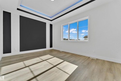 Spacious room featuring wood-finish flooring, a tray ceiling with integrated lighting, and a large multi-pane window - 4409 35 Street, Beaumont, AB - Indoor Photo Showing Other Room