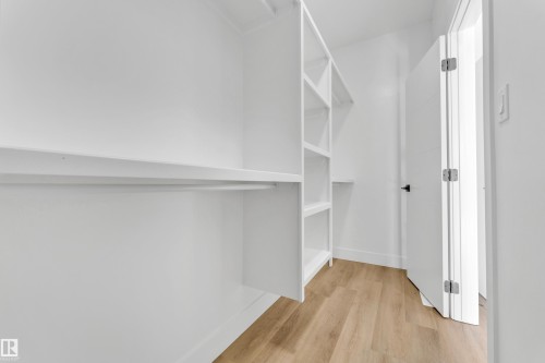 Walk-in closet featuring built-in shelving, hanging rods, light wood-finish flooring, white baseboards, and a white door with black hardware - 4409 35 Street, Beaumont, AB - Indoor With Storage