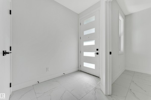 Entry area featuring a modern door with frosted glass panels, white baseboards, a single window, and large format marble-look tile flooring - 4409 35 Street, Beaumont, AB - Indoor Photo Showing Other Room