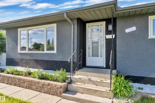 Exterior featuring gray stucco siding, black brick accents, and a white front entry door - 8104 135 Avenue, Edmonton, AB 