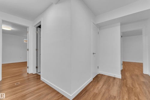 Interior hallway featuring wood-finish flooring, white painted walls, and white trim - 8104 135 Avenue, Edmonton, AB 