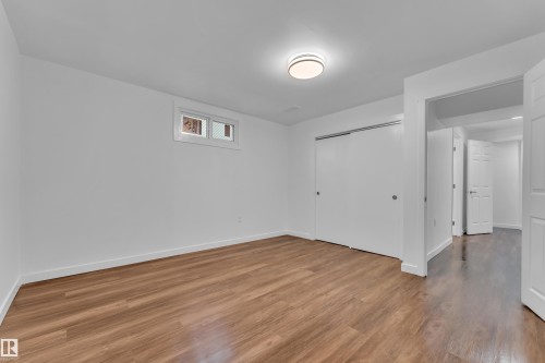 Spacious room featuring wood-finish flooring, crisp white walls, and a recessed window - 8104 135 Avenue, Edmonton, AB 