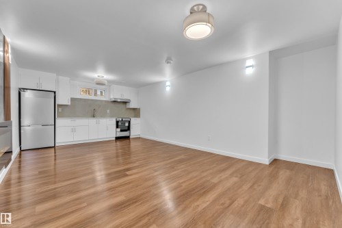 Open-concept living space featuring wood-finish flooring, white cabinetry, stainless steel appliances, a modern sink, and recessed and flush-mount lighting fixtures - 8104 135 Avenue, Edmonton, AB 