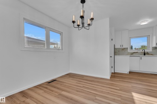 Open-concept living area with light wood-finish flooring, a modern black chandelier, and white window trim - 8104 135 Avenue, Edmonton, AB 