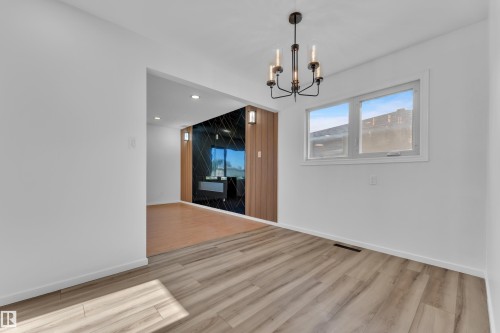 Bright room featuring wood-finish flooring, a modern black chandelier, and white trim - 8104 135 Avenue, Edmonton, AB 