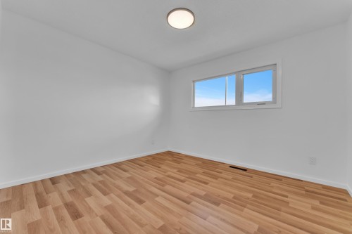 Bright room featuring wood-finish flooring, white walls, and a large horizontal window providing natural light - 8104 135 Avenue, Edmonton, AB 
