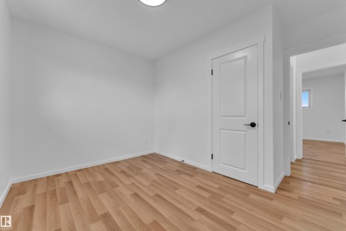 Room featuring light wood-finish flooring, white walls, and a white interior door with matte black hardware - 8104 135 Avenue, Edmonton, AB 