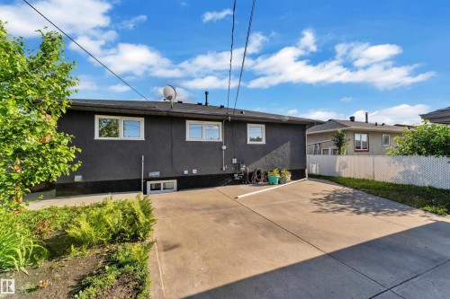 Rear exterior featuring dark stucco siding, white-framed windows, and a concrete driveway - 8104 135 Avenue, Edmonton, AB 
