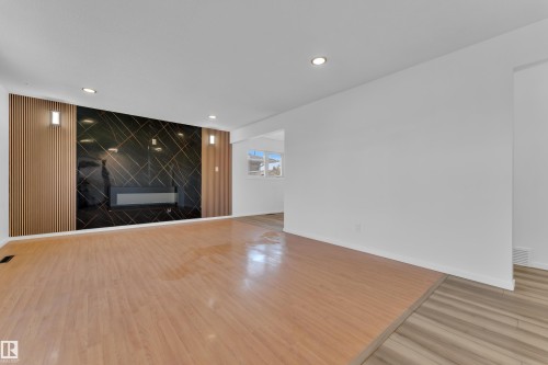 Living area featuring wood-finish flooring, a contemporary fireplace, and a striking black and gold accent wall - 8104 135 Avenue, Edmonton, AB 