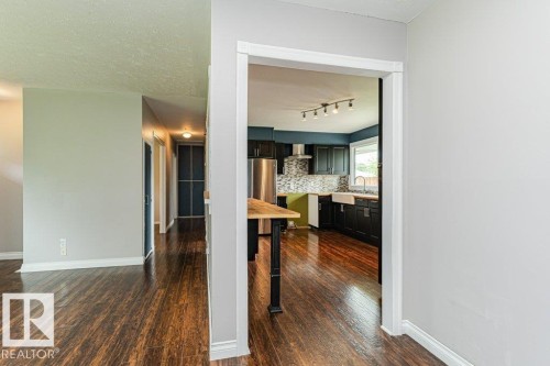 Kitchen featuring dark cabinetry, stainless steel appliances, a farmhouse sink, and a mosaic tile backsplash - 13411 140 Street, Edmonton, AB 